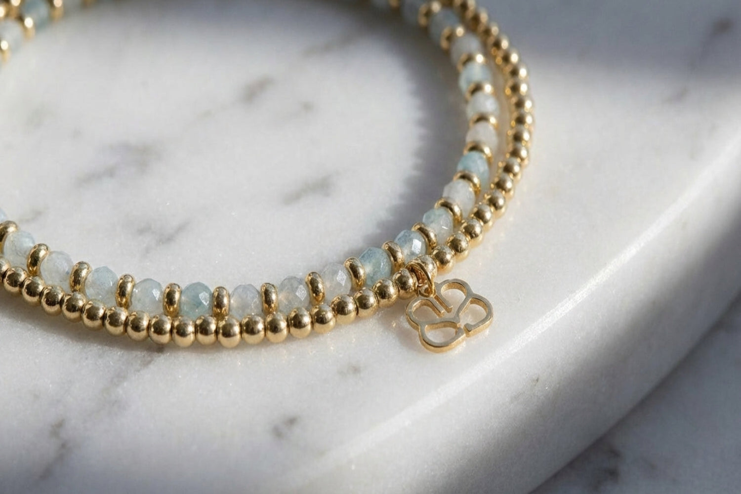 Bracelet resting on marble surface, highlighting its faceted aquamarine beads and gold details with textures and reflections.