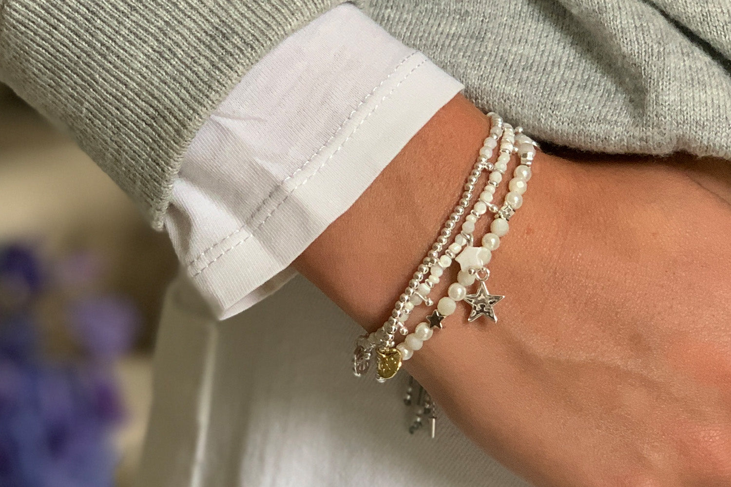 Close-up of a white and silver star stacking bracelet set styled with a casual grey jumper.